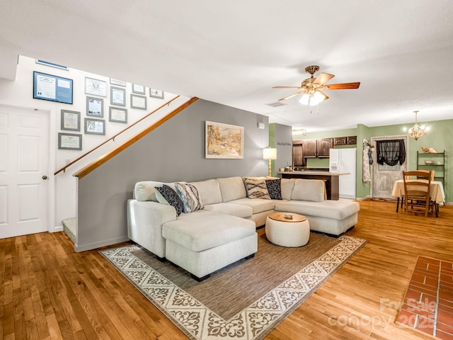 living room featuring light wood-style floors, a chandelier, stairway, ceiling fan, and baseboards