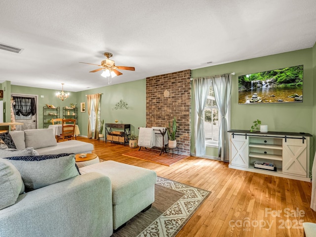 living area featuring wood-type flooring, a ceiling fan, a chandelier, a textured ceiling, and baseboards