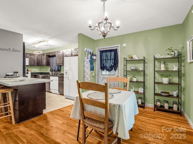 dining area featuring a chandelier, light wood-type flooring, a textured ceiling, and baseboards