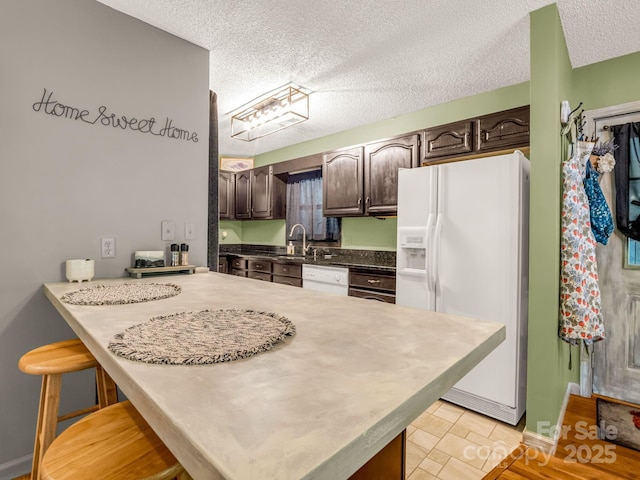 kitchen featuring white appliances, dark brown cabinets, a kitchen breakfast bar, a textured ceiling, and baseboards