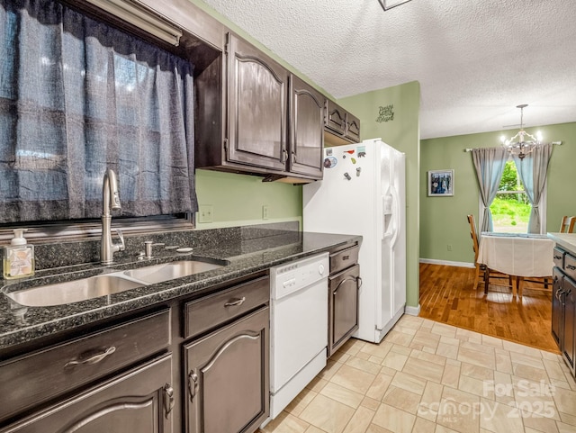 kitchen featuring white appliances, a sink, dark brown cabinetry, a chandelier, and baseboards