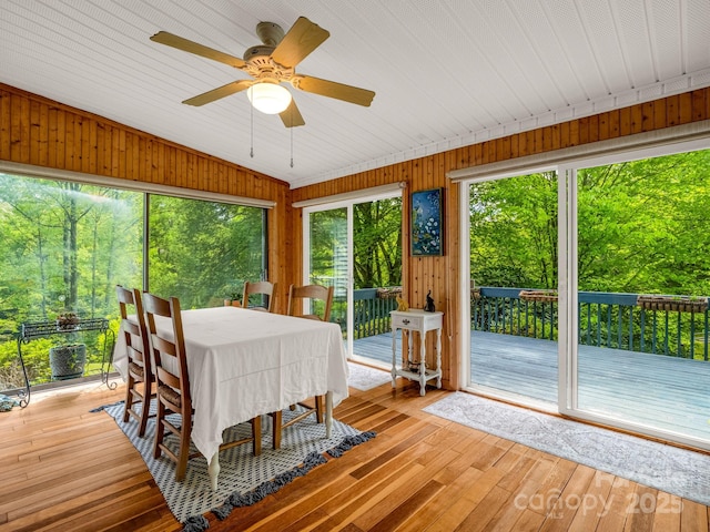 sunroom / solarium featuring healthy amount of natural light, a wooden deck, wood-type flooring, wooden walls, and lofted ceiling