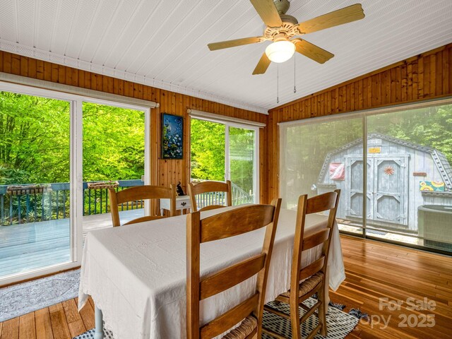 dining area featuring vaulted ceiling, hardwood / wood-style flooring, wooden walls, and a ceiling fan