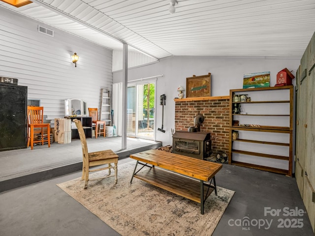 living room with a wood stove, vaulted ceiling, and concrete floors