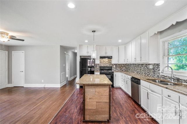 kitchen with black appliances, a sink, exhaust hood, backsplash, and light stone countertops