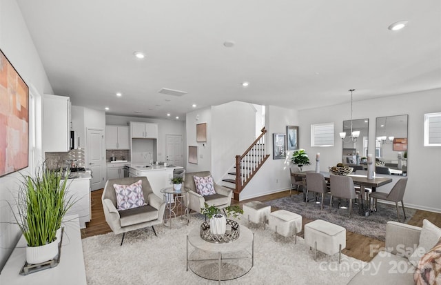 living area with wood finished floors, stairway, recessed lighting, baseboards, and a chandelier