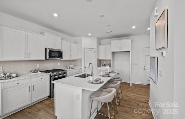 kitchen featuring appliances with stainless steel finishes, a sink, white cabinets, tasteful backsplash, and wood finished floors