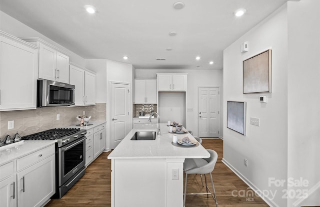 kitchen with appliances with stainless steel finishes, a sink, white cabinetry, backsplash, and dark wood-style flooring