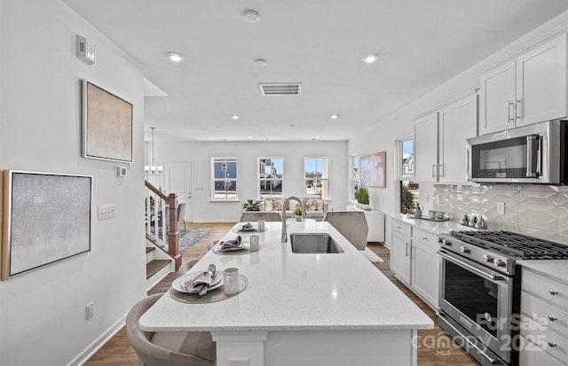 kitchen with stainless steel appliances, a sink, white cabinetry, a center island with sink, and backsplash