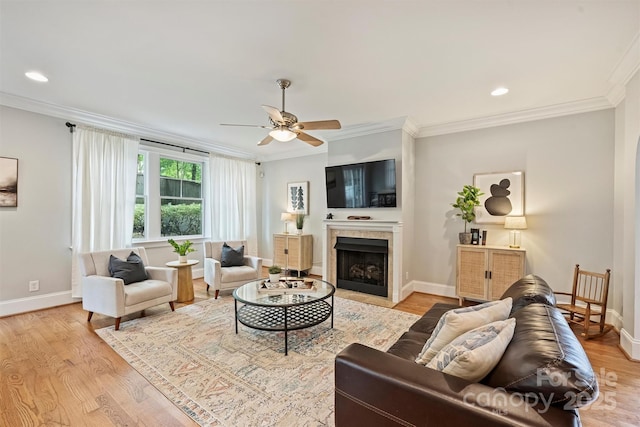 living area featuring ornamental molding, ceiling fan, light wood-style floors, baseboards, and a fireplace