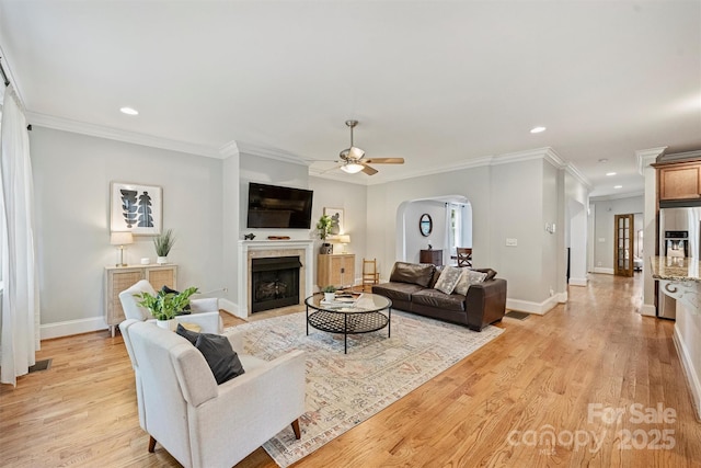 living room with arched walkways, a ceiling fan, recessed lighting, ornamental molding, and a fireplace