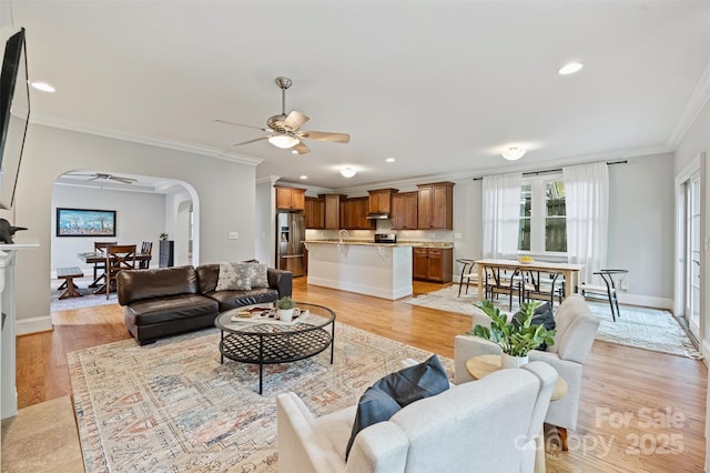 living area featuring a ceiling fan, crown molding, arched walkways, light wood finished floors, and recessed lighting