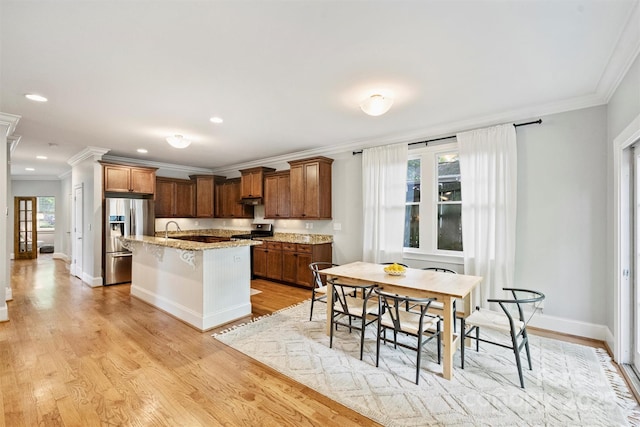kitchen with stainless steel refrigerator with ice dispenser, crown molding, a breakfast bar, an island with sink, and light stone counters