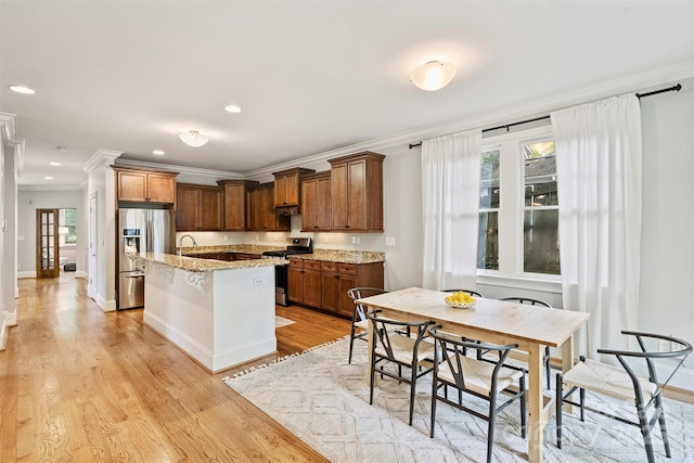 kitchen with stainless steel appliances, ornamental molding, light wood-style flooring, a kitchen island with sink, and light stone counters