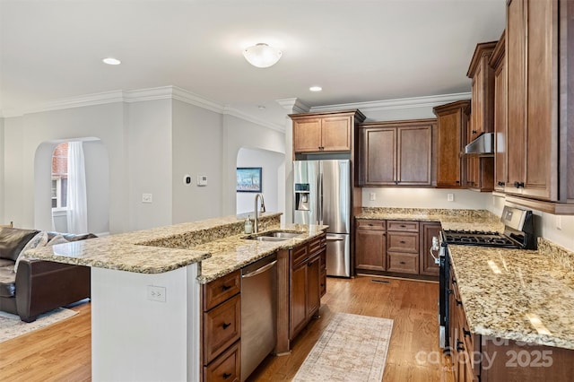 kitchen featuring stainless steel appliances, arched walkways, a sink, under cabinet range hood, and crown molding