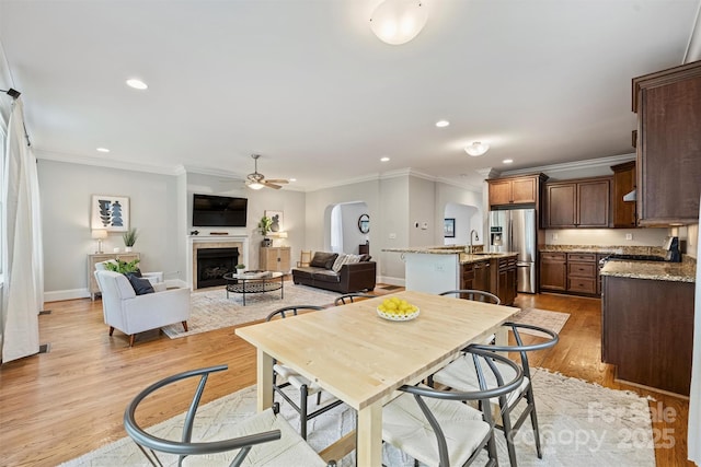 dining area with arched walkways, crown molding, recessed lighting, ceiling fan, and a fireplace