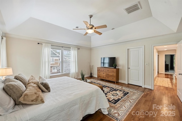 bedroom with a tray ceiling, wood finished floors, a ceiling fan, crown molding, and baseboards