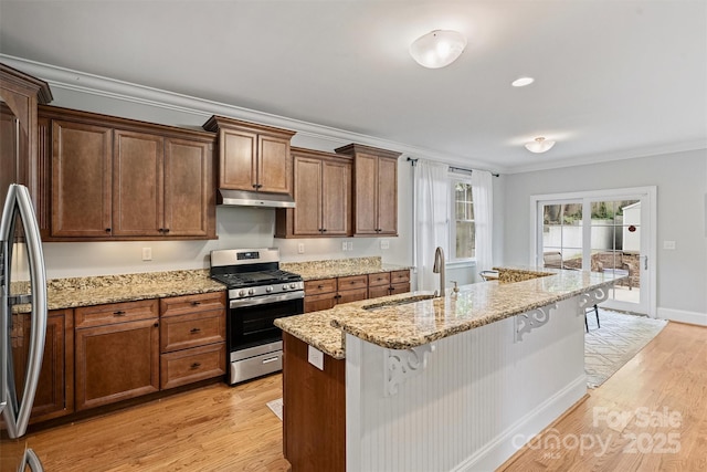 kitchen featuring stainless steel appliances, a sink, under cabinet range hood, crown molding, and light wood-type flooring