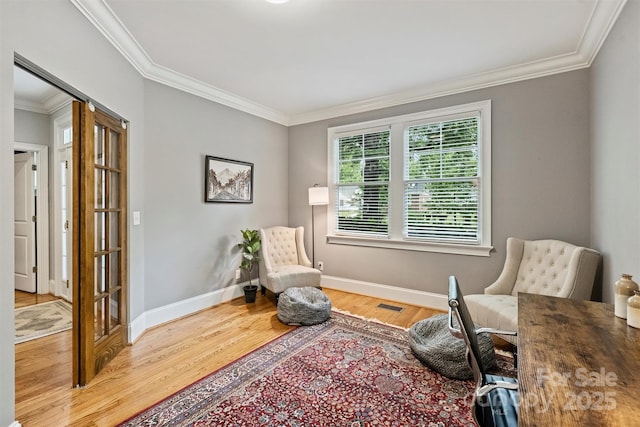 living area with wood finished floors, ornamental molding, and baseboards