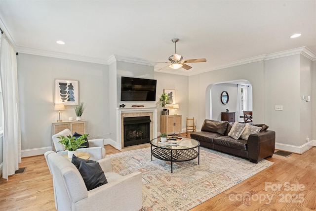 living room featuring arched walkways, a ceiling fan, baseboards, ornamental molding, and light wood finished floors