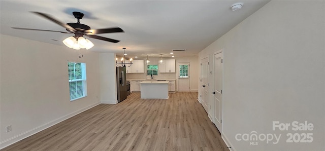 kitchen featuring stainless steel fridge, light wood-type flooring, a kitchen island, light countertops, and white cabinetry