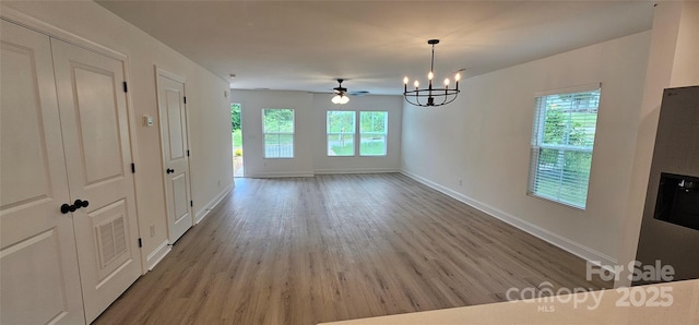 unfurnished dining area featuring plenty of natural light, light wood finished floors, a chandelier, and baseboards