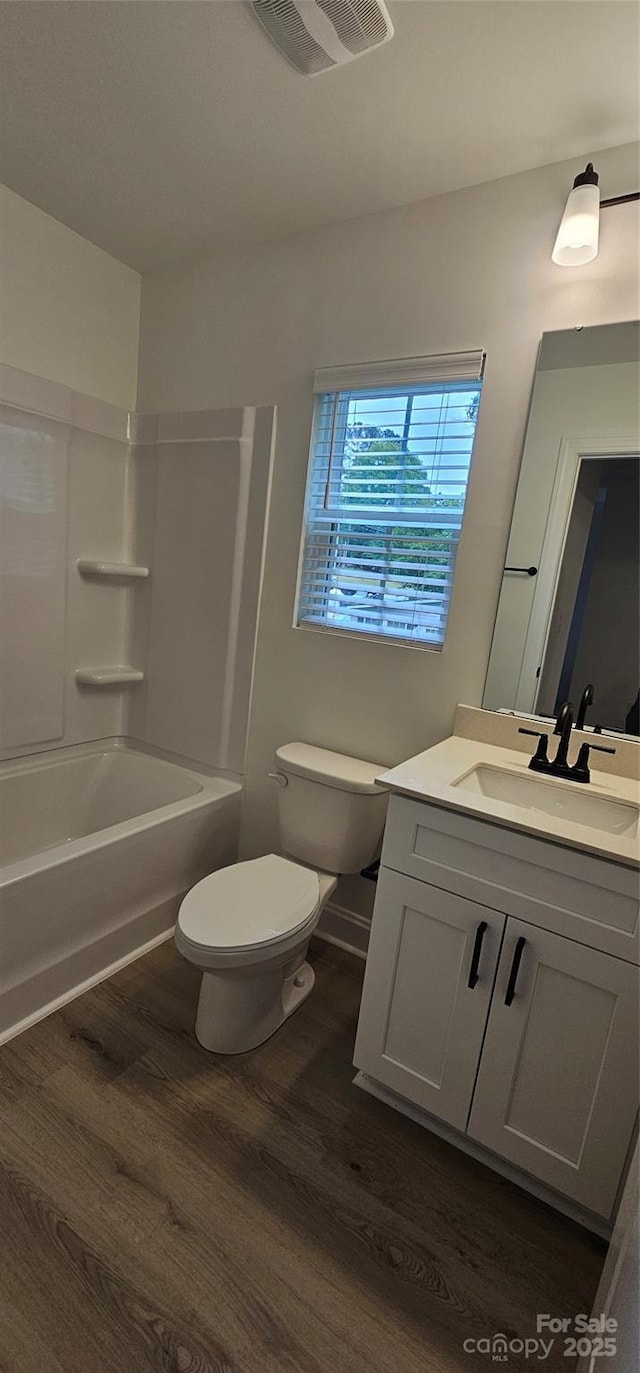bathroom featuring wood finished floors, toilet, vanity, and tub / shower combination