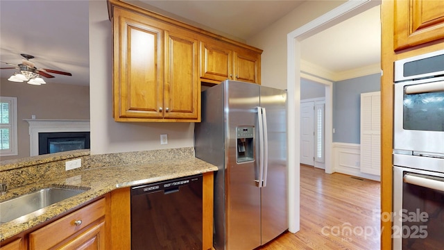 kitchen featuring stainless steel appliances, ceiling fan, light wood-style floors, light stone counters, and a glass covered fireplace