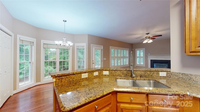 kitchen with a sink, brown cabinets, light stone counters, a ceiling fan, and wood finished floors