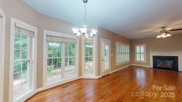 unfurnished living room featuring wood finished floors, a chandelier, baseboards, a fireplace with flush hearth, and ceiling fan
