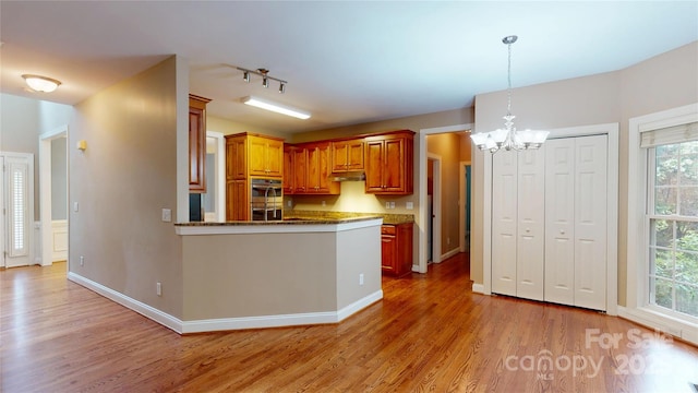 kitchen with a chandelier, light wood-style floors, stainless steel double oven, and pendant lighting