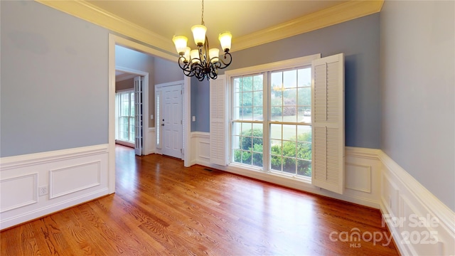 unfurnished dining area featuring a chandelier, ornamental molding, a wainscoted wall, a decorative wall, and light wood-style floors
