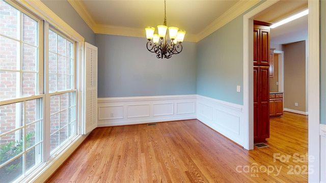 unfurnished room featuring a chandelier, light wood-type flooring, ornamental molding, and wainscoting