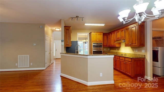 kitchen featuring a chandelier, under cabinet range hood, light wood-style flooring, appliances with stainless steel finishes, and stone counters