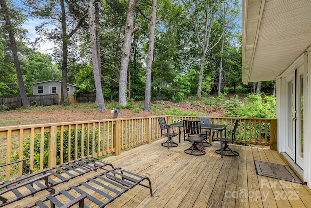 wooden deck with outdoor dining space, fence, and view of wooded area