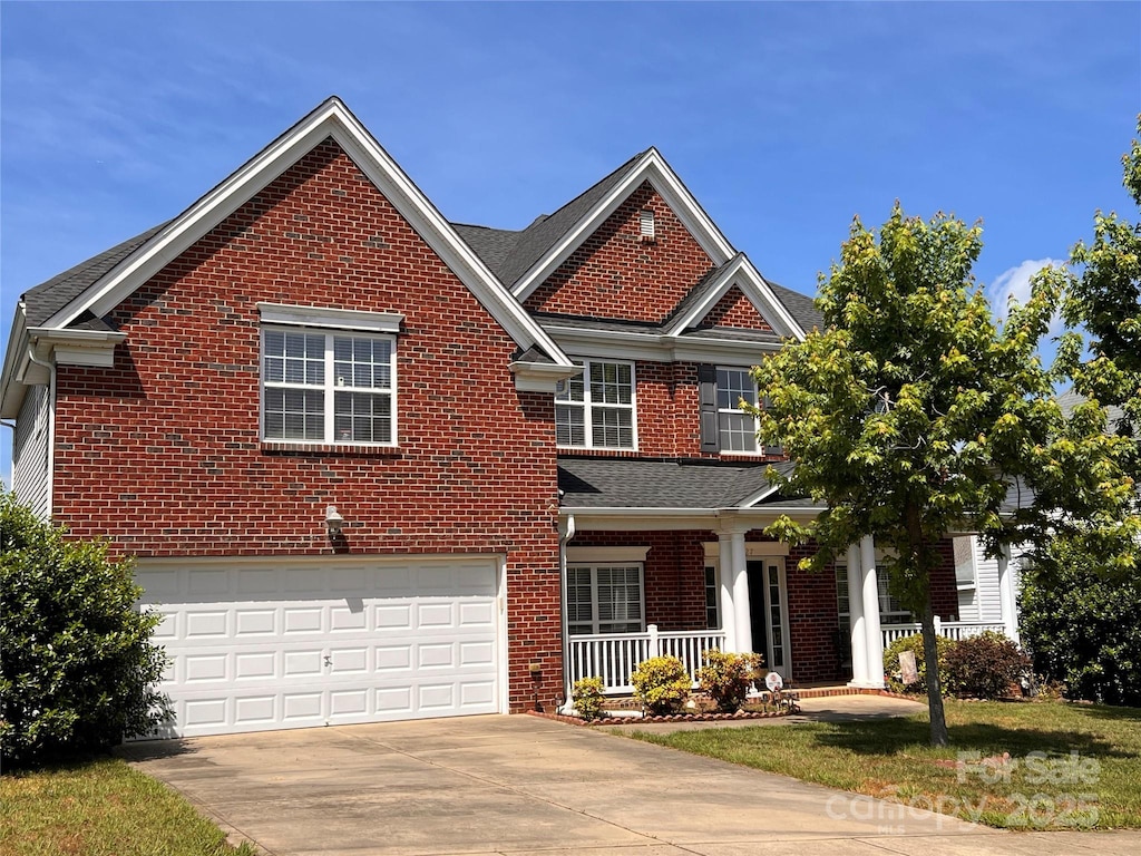 traditional-style house featuring brick siding, a porch, concrete driveway, an attached garage, and a front yard
