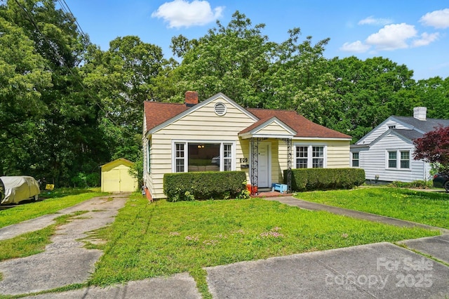 bungalow-style house with a front lawn, a storage shed, and a chimney