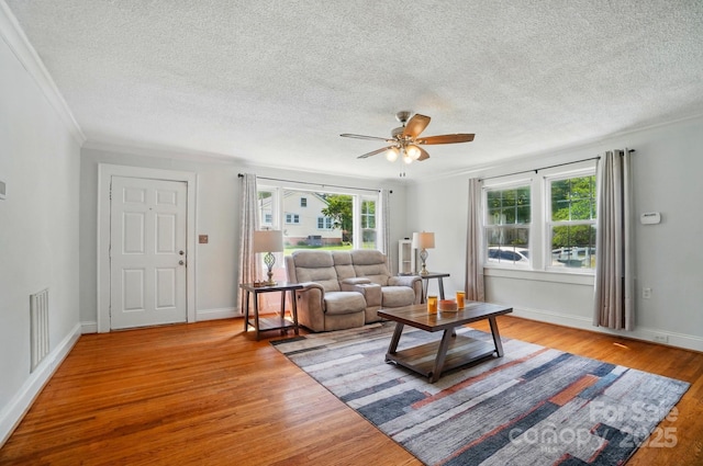 living area featuring a ceiling fan, a textured ceiling, wood finished floors, ornamental molding, and baseboards