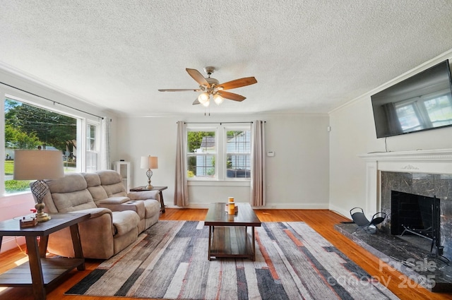 living area with healthy amount of natural light, a premium fireplace, a ceiling fan, wood finished floors, and crown molding