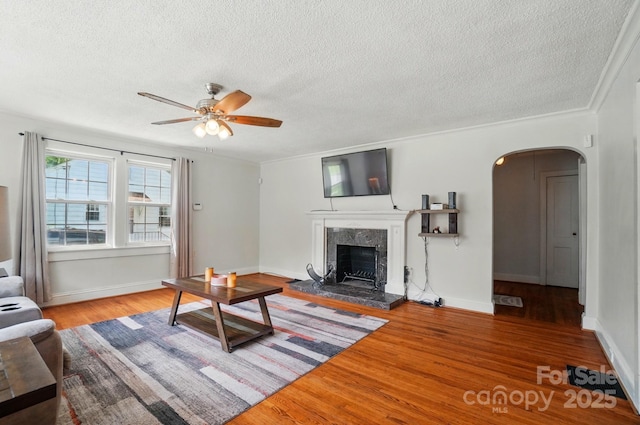 living room with arched walkways, a textured ceiling, wood finished floors, ceiling fan, and a fireplace