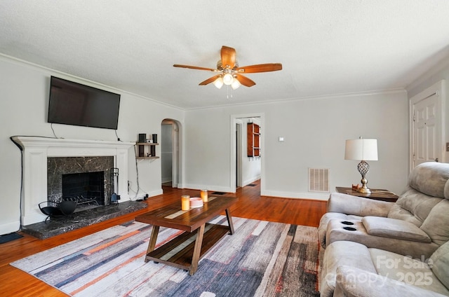living room featuring arched walkways, wood finished floors, a ceiling fan, ornamental molding, and a fireplace