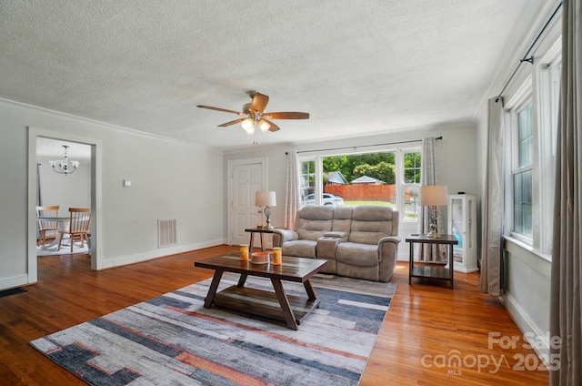 living area with a textured ceiling, a ceiling fan, wood finished floors, crown molding, and a chandelier