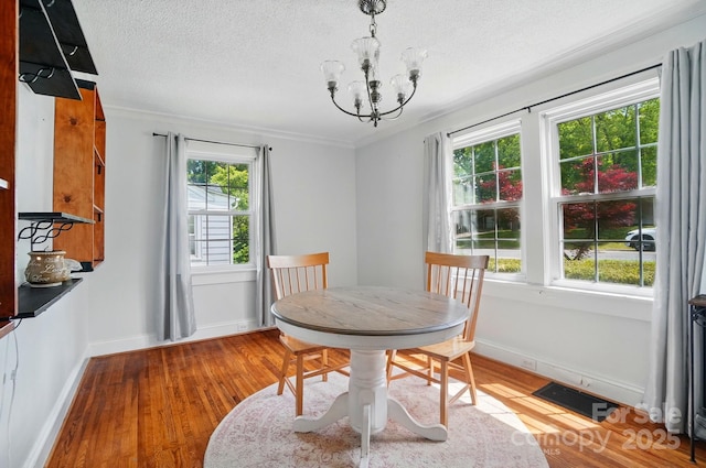 dining area featuring a chandelier, light wood-type flooring, a textured ceiling, baseboards, and ornamental molding