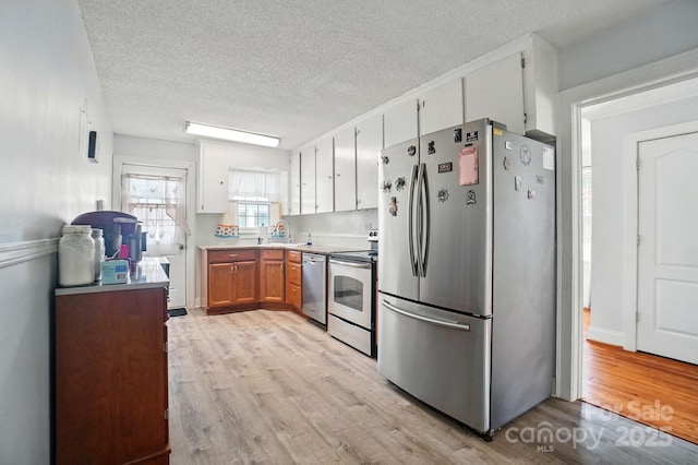 kitchen featuring appliances with stainless steel finishes, light wood finished floors, a textured ceiling, light countertops, and white cabinets