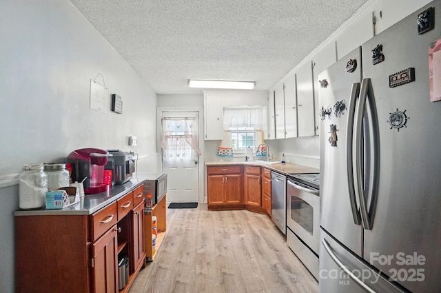 kitchen featuring appliances with stainless steel finishes, light wood-style floors, a textured ceiling, a sink, and light countertops