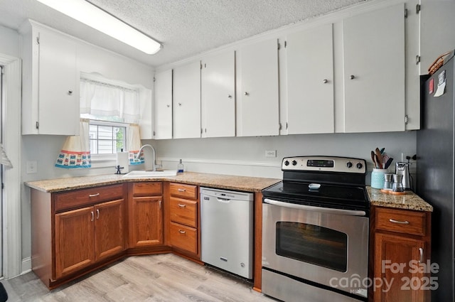 kitchen with stainless steel appliances, a sink, a textured ceiling, light wood-type flooring, and white cabinetry