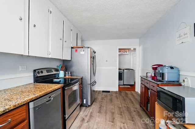kitchen with appliances with stainless steel finishes, light wood finished floors, a textured ceiling, white cabinetry, and washer and dryer