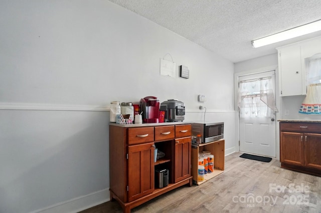kitchen with stainless steel microwave, light wood-style flooring, a textured ceiling, light countertops, and brown cabinets
