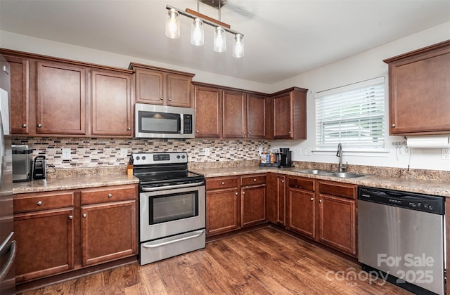 kitchen with stainless steel appliances, a sink, dark wood-style flooring, and decorative backsplash