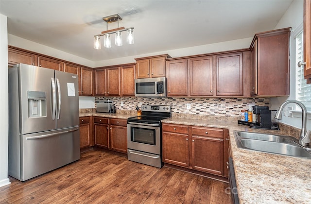 kitchen with stainless steel appliances, a sink, dark wood-style flooring, backsplash, and brown cabinets